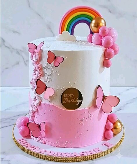 Pink two-tier cake with butterflies, a rainbow topper and gold pearls