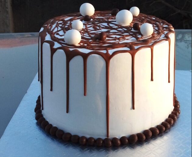 White cake with a chocolate drip and chocolate truffle border