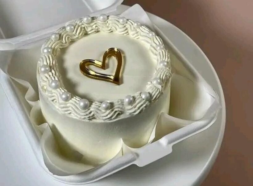 Small white cake with pearl piping and a gold heart topper, boxed