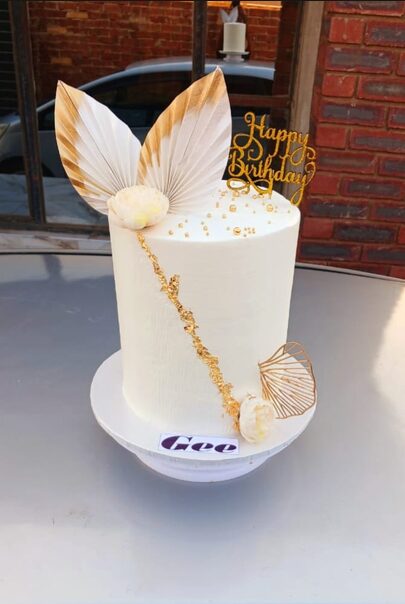 White cake with gold leaf detailing and a Happy Birthday topper