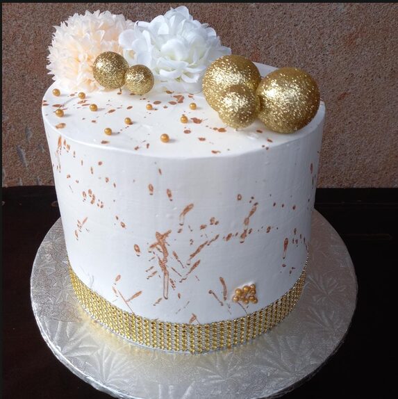 White cake with rose-gold splatter, gold baubles and fabric flowers
