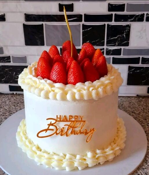 White birthday cake topped with fresh strawberries and a gold candle
